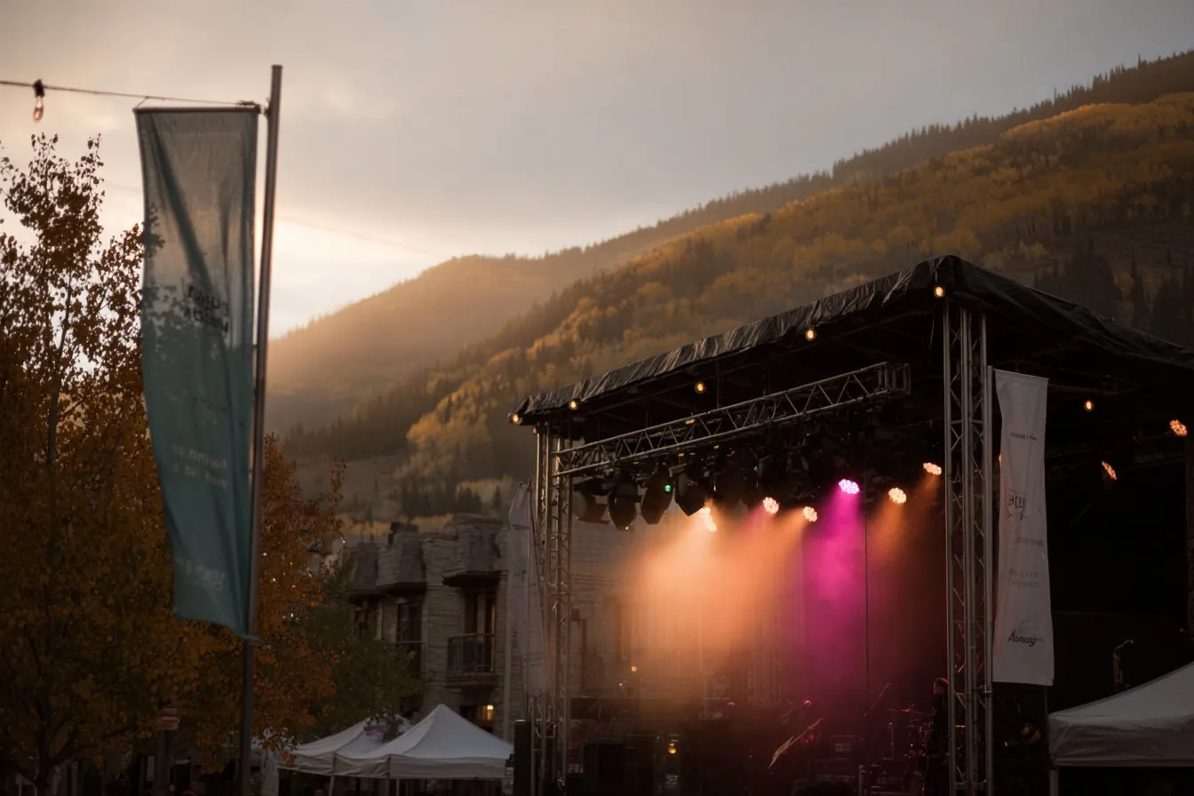 Outdoor festival stage with pink and amber lights at golden hour below hills of golden fall aspens