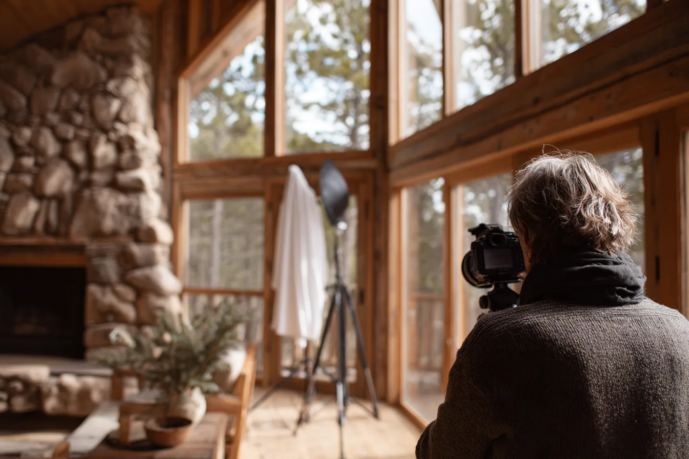 Photographer with a camera on a tripod shooting a cabin great room with a stone fireplace